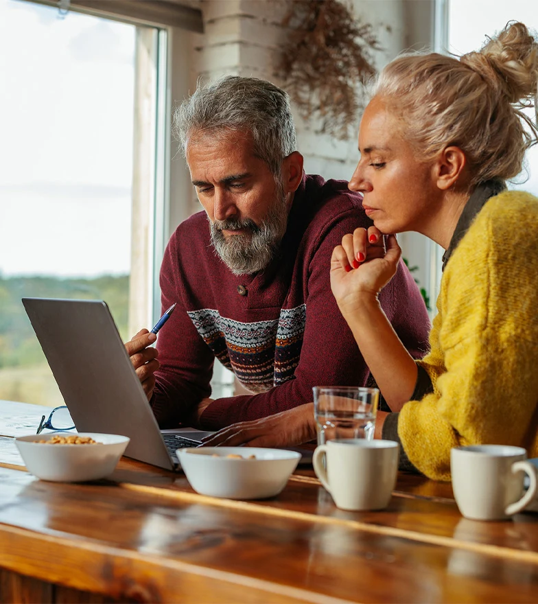Middle aged couple on breakfast bar looking at laptop